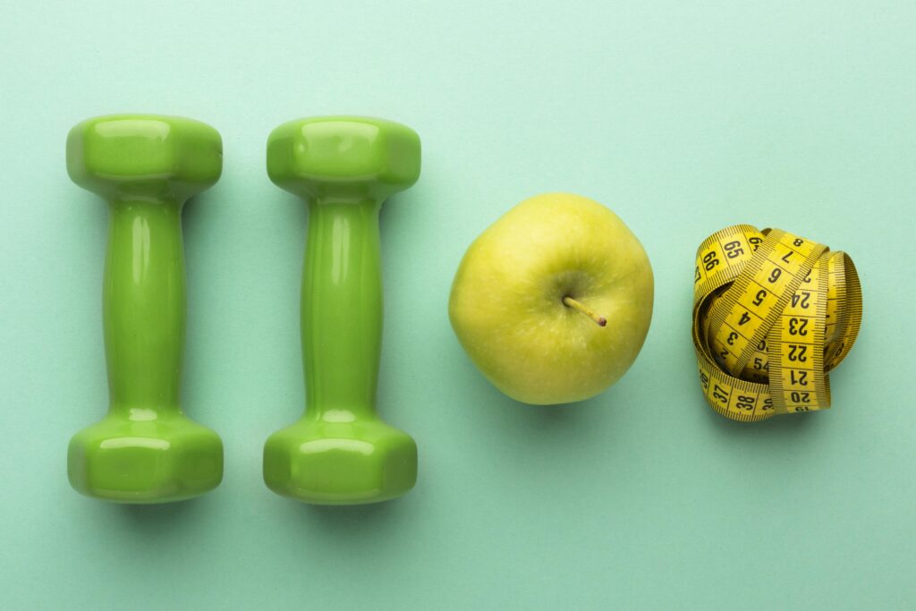 a green dumbbells and an apple next to a measuring tape